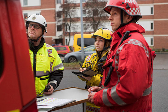 Tre brandmän med full utrustning tittar på något